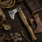 Carved Viking-style axe with leather sheath, compass, coins, rope, and vintage journal on a dark wooden surface.
