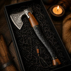 An engraved Viking-style axe with a leather-wrapped handle, presented in a black gift box with a lit candle nearby.