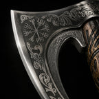 engraved metal axe head featuring Nordic-inspired symbols and decorative patterns, with a carved wooden handle partially visible against a black background.