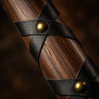Close-up of dark wood handle wrapped in crisscrossed black leather with brass rivets